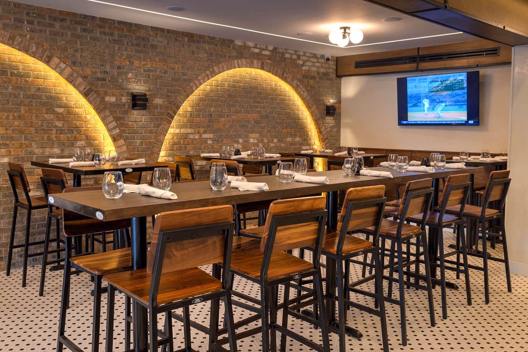 Warm, modern dining room featuring high-top seating, ambient arch lighting, a full-service bar, and TVs for sports and entertainment.