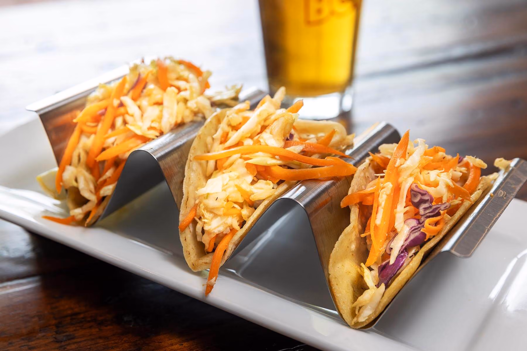 Three crispy fish tacos topped with cabbage slaw and served with a cold draft beer.